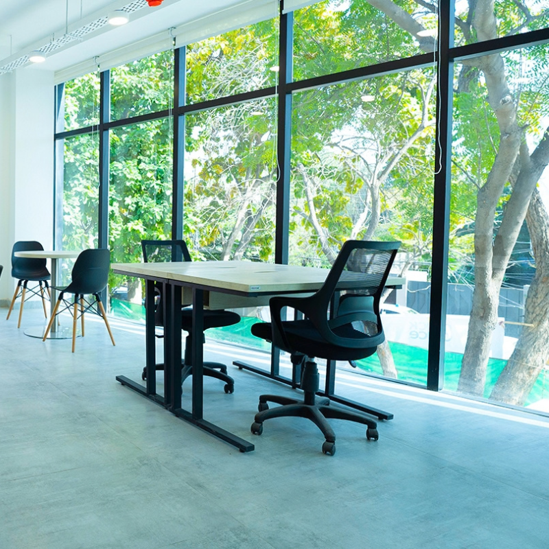 Office desk with black chairs beside floor-to-ceiling windows overlooking green trees in a bright QuickOffice space