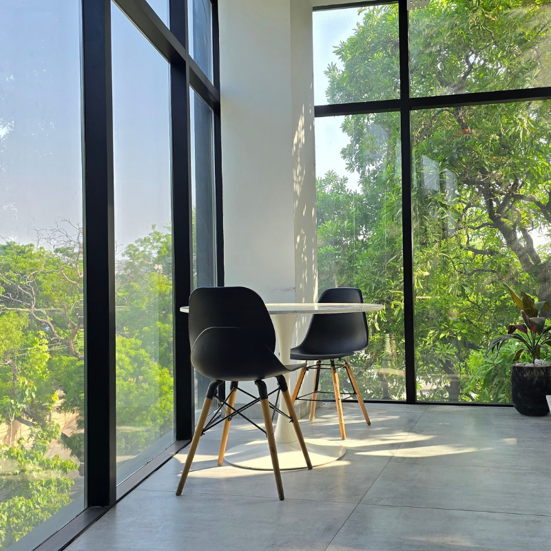 Small round table with two black chairs in a sunlit window corner with tree views at QuickOffice