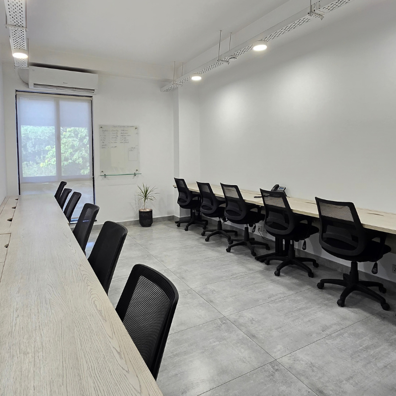 Private office with a long wooden desk, black chairs along one side, and a window letting in daylight