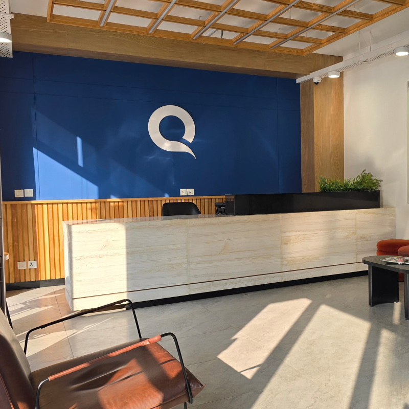 Reception area at QuickOffice MM Alam with a blue logo wall, timber paneling and a stone-finish front desk