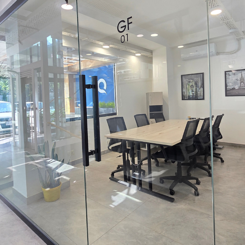 Glass-walled room GF 01 with a long wooden table and black mesh chairs at QuickOffice MM Alam